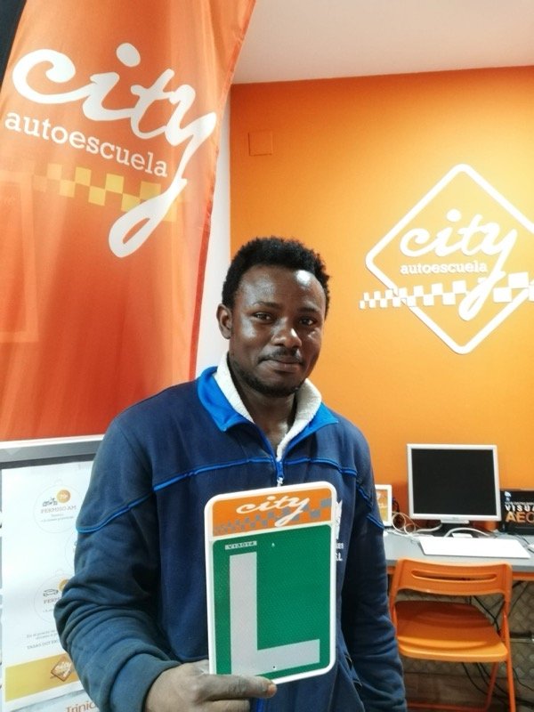 Alumno de City Autoescuela con la placa L tras aprobar, junto a la banderola del local