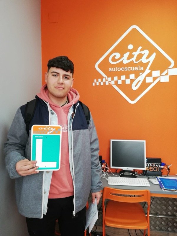 Alumno de City Autoescuela con la placa L tras aprobar, delante del logo de la escuela